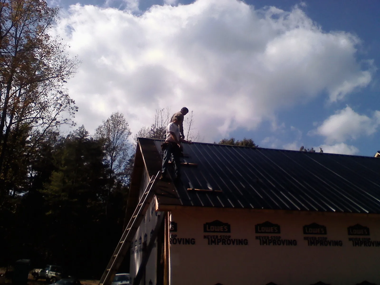 Roofer fastening dark metal panels high against a cloudy sky, from a Roof Inspection job in Sciota