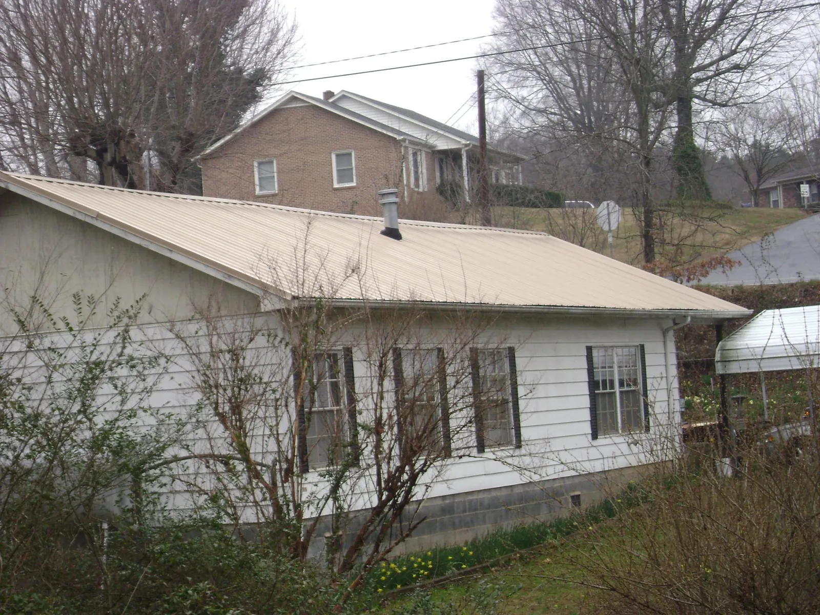 Tan metal roof on a white sided house set into a hillside — Commercial Roofing by Roofing Brothers in Sciota